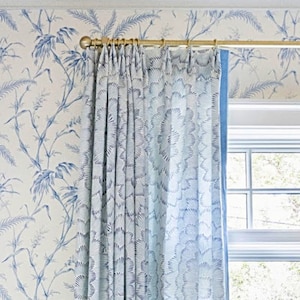 May include: White and blue patterned curtains with a gold curtain rod hanging from a white ceiling. The curtains are drawn and the window behind them is visible.