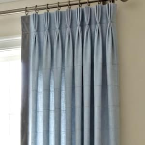 May include: A light blue curtain panel featuring a subtle grid pattern and a vertical row of pinch pleats at the top. The curtain is suspended from a metallic curtain rod with decorative finials using small metal rings attached to the fabric.
