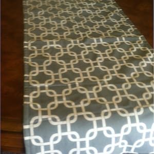 May include: A gray and white table runner with a geometric pattern. The pattern is made up of interlocking circles and squares.