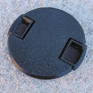 May include: A black, circular object with two rectangular protrusions. The object has a textured surface and is set against a grey, speckled background. The protrusions have a ridged interior.