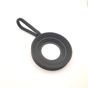 May include: A black, circular object with a handle. The object has a ridged design around the outer edge and a large, open centre. The handle is a loop of the same black material.
