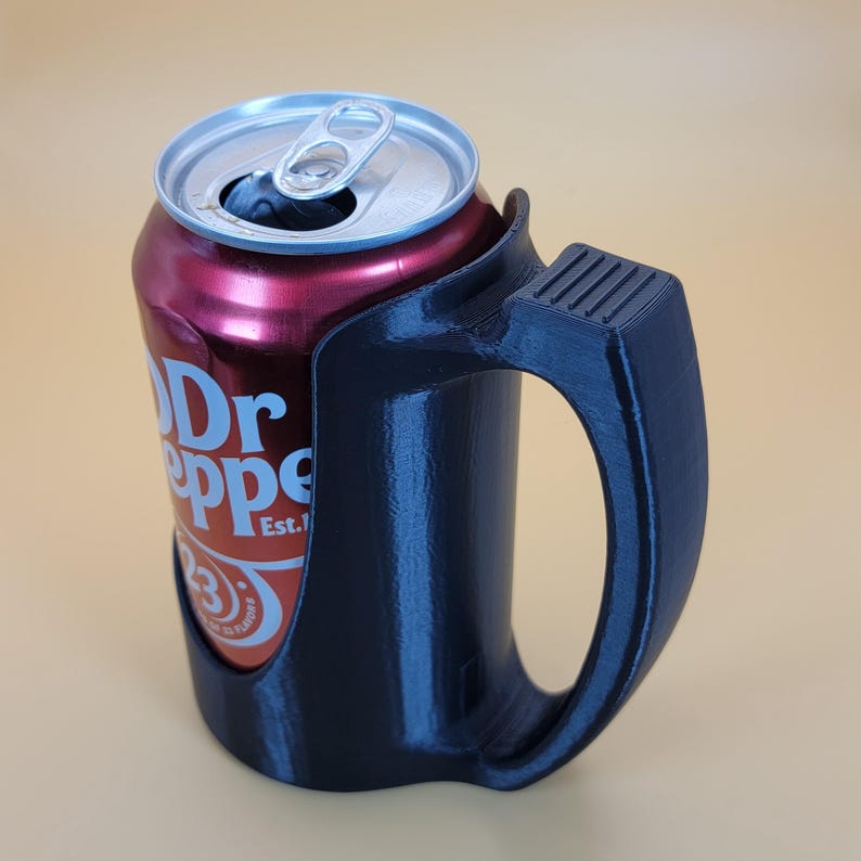 May include: A black 3D printed can holder with a handle. A can of Dr Pepper is in the holder. The can is red with white lettering that says "Dr Pepper Est. 1885".