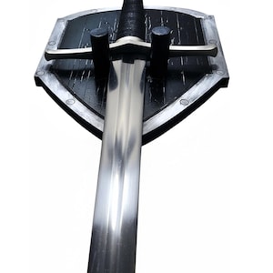 May include: A long, double-edged steel sword with a silver-toned crossguard and a black-wrapped grip, mounted vertically on a black, shield-shaped wooden plaque with a silver-painted border and visible wood grain texture throughout the surface.