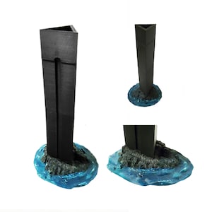 May include: A black triangular tower with a split down the center, standing on a blue and gray base that resembles water. The tower is made of a material that looks like plastic or resin.