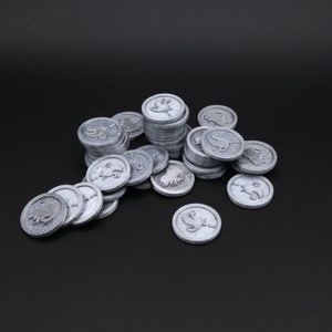 May include: A pile of silver-colored metal coins with a design on each side. The coins are arranged in a random pattern.