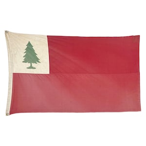 May include: A rectangular flag with a white canton featuring a green pine tree and a red field. The flag has eyelets on the left side for hanging. The flag is made of fabric and has a vintage appearance.