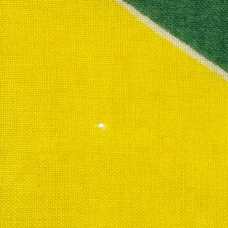 Pode incluir: Close-up de um tecido amarelo com uma trama texturizada. Uma pequena mancha branca brilhante &eacute; vis&iacute;vel na superf&iacute;cie amarela. O canto superior direito apresenta uma se&ccedil;&atilde;o diagonal de tecido verde, separada por uma faixa branca.