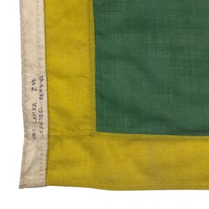 Puede incluir: Primer plano de una bandera con un esquema de color amarillo y verde. La bandera tiene una etiqueta blanca cosida en la esquina que dice "SRI LANKA 2 YD CARTERS READING."