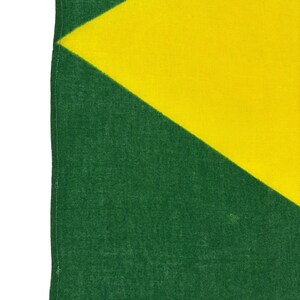 Pode incluir: Close-up de uma bandeira verde e amarela. A bandeira tem um tri&acirc;ngulo amarelo diagonal sobre um fundo verde. O tecido tem uma apar&ecirc;ncia texturizada.