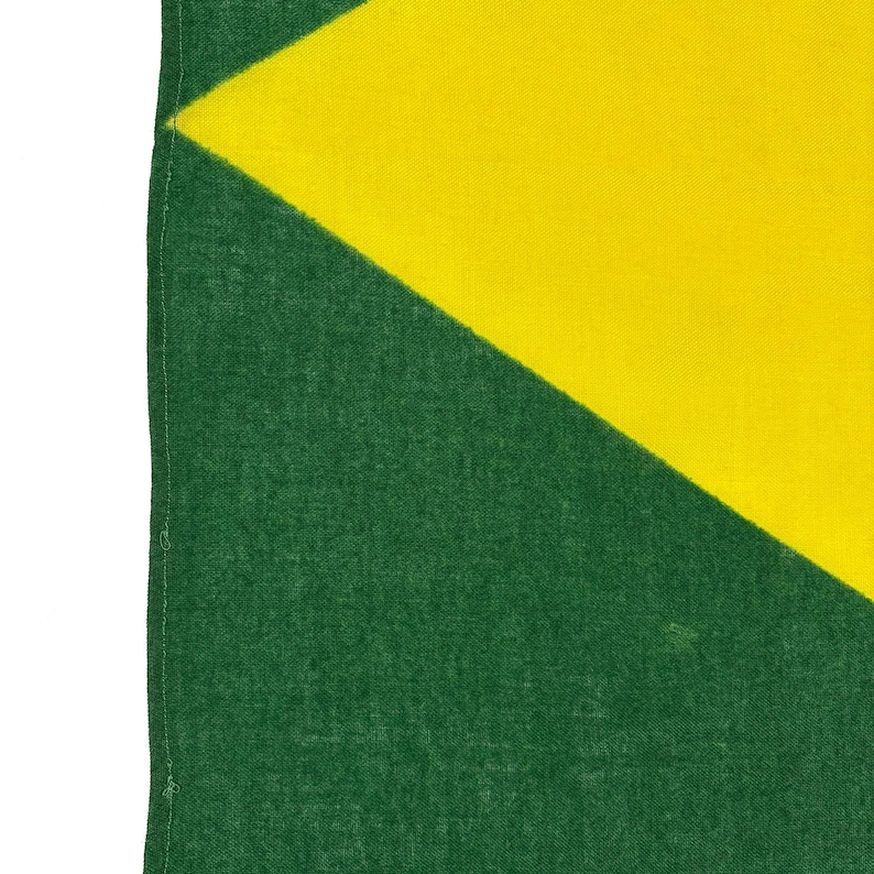 Pode incluir: Close-up de uma bandeira verde e amarela. A bandeira tem um tri&acirc;ngulo amarelo diagonal sobre um fundo verde. O tecido tem uma apar&ecirc;ncia texturizada.