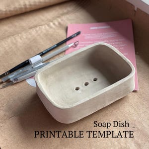 May include: A printable template for a soap dish. The template is a light beige colour and has three drainage holes. The template is on a brown surface.