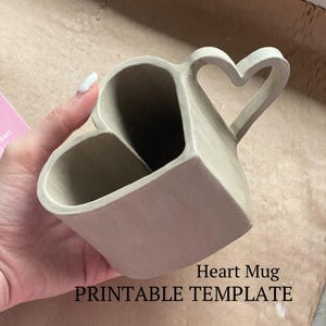 May include: A printable template for a heart-shaped mug with a heart-shaped handle. The template is made of light brown clay.
