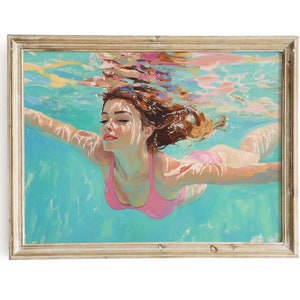 Puede incluir: Una pintura enmarcada de una mujer con cabello largo y castaño nadando bajo el agua. Lleva un traje de baño rosa y el agua es de un color turquesa vibrante.
