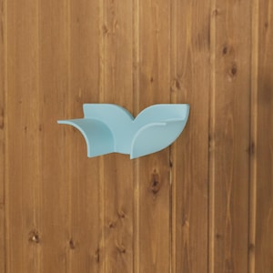 May include: A light blue wall-mounted shelf featuring a curved, wing-like silhouette with two symmetrical, upward-sweeping side panels and a flat central surface, designed for mounting on a vertical surface to provide a small display area.