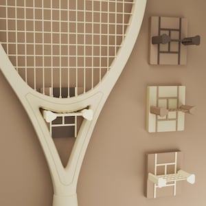 Könnte beinhalten: Ein Tennisschläger und drei Wandhalterungen für Tennisbälle in einer neutralen Farbpalette. Der Schläger ist cremefarben mit einem Saitennetz. Die Halterungen sind rechteckig mit einem Gitterdesign und einem gebogenen Arm.