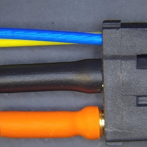May include: A close-up of a black electrical connector with three wires attached. The wires are blue, yellow, and orange. The connector has a gold-colored metal pin.