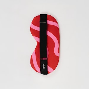 Peut inclure: Un masque de sommeil avec une base rouge et des rayures roses ondulées. Le masque comprend une sangle élastique noire avec une boucle réglable et le mot Volta imprimé en blanc sur la sangle. Le design est symétrique et profilé pour la couvrance.