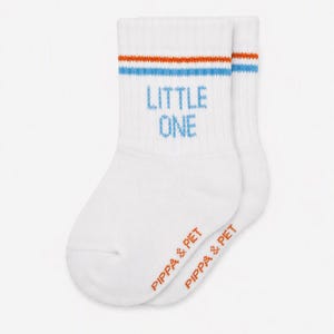 Puede incluir: Un par de calcetines blancos con el texto LITTLE ONE en azul en el tobillo. La parte superior de los calcetines tiene dos finas rayas horizontales en naranja y azul. El texto PIPPA & PIET está impreso en naranja en la zona del pie.