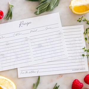 Two recipe cards sit on a kitchen counter halfway overlapping. One recipe card displays the front of the card and the second recipe card is turned over to display the back of the card. Both sides have a beautiful grey and white floral design.
