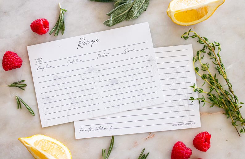 Two recipe cards sit on a kitchen counter halfway overlapping. One recipe card displays the front of the card and the second recipe card is turned over to display the back of the card. Both sides have a beautiful grey and white floral design.