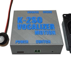 May include: A gray 3D-printed electronic control box with blue embossed text reading K-2SO VOCALIZER MOTION, POWER, and SWITCH. It includes two wired sensors, one with a white dome, and a separate black rectangular speaker unit with red and black wires.