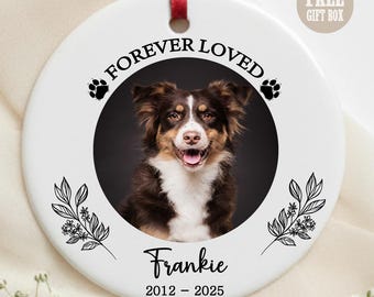 May include: A white ceramic ornament with a photo of a brown and white dog, the text "FOREVER LOVED", paw prints, floral accents, and the name "Frankie" with the years 2012-2025. A red ribbon is attached for hanging.