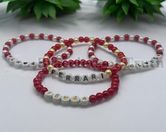 Puede incluir: Tres pulseras de cuentas rojas y blancas con detalles dorados. Las pulseras deletrean las palabras "Ferrari", "H4" y "Truth".