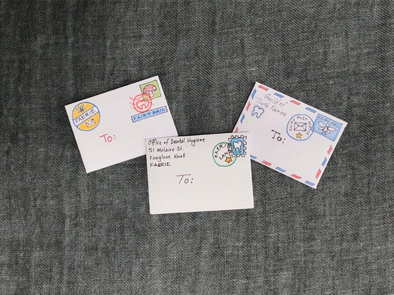 K&ouml;nnte beinhalten: Drei wei&szlig;e Umschl&auml;ge mit handgezeichneten Illustrationen von Feen, einem Zahn und einem Pilz. Die Umschl&auml;ge sind an "An :" adressiert und haben Briefmarken mit den Worten "Fairy Mail" und "Fairy Post Service".