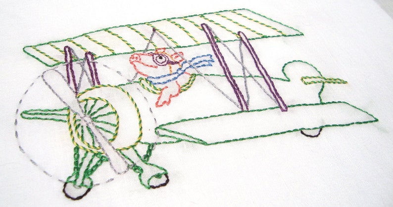 May include: Embroidered design of a green and yellow biplane with a red and orange pig wearing goggles and a blue scarf in the cockpit.