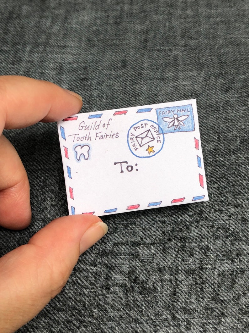 K&ouml;nnte beinhalten: Ein wei&szlig;er Umschlag mit roten und blauen Streifen. Der Umschlag hat eine Zeichnung eines Zahns und den Text "Guild of Tooth Fairies". Au&szlig;erdem hat er eine Briefmarke mit einer Fee und dem Text "Fairy Post Office" und "Fairy Mail". Der Umschlag ist adressiert mit "To:"