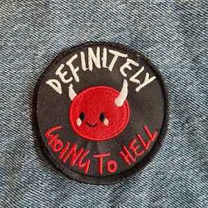 May include: A circular embroidered patch with a black background featuring a red devil character with white horns and a smiling face. The white text reads DEFINITELY and the red text reads GOING TO HELL, arranged in a curve around the character.