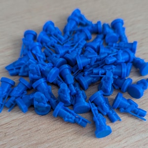 May include: A pile of blue plastic miniature figures, possibly for a board game or war game. The figures are all in the same pose, standing upright with their arms at their sides.