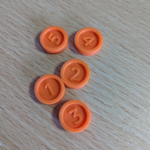 May include: Five orange plastic tokens with numbers 1 through 5 printed on them.