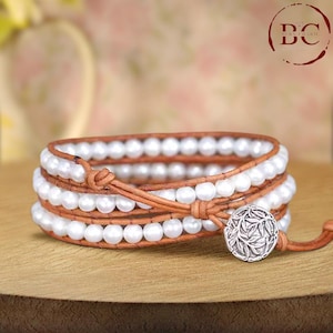 May include: A triple wrap leather bracelet with white pearls and a silver charm featuring a leaf design.
