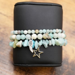 May include: A stack of three bracelets made with light blue and white beads, with a silver star charm and a silver wing charm.