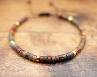 May include: A multi-colored beaded bracelet with a brown, red, and green color scheme. The bracelet has gold accents and a sliding knot closure.