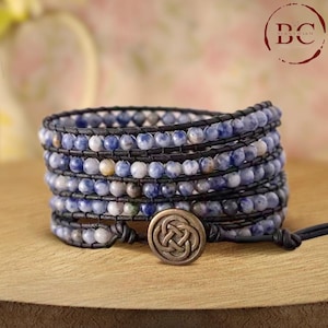 May include: A multi-strand wrap bracelet with blue and white beads, black leather cord, and a bronze Celtic knot closure.