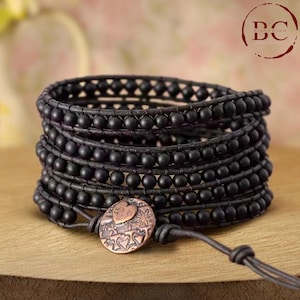 May include: Black leather wrap bracelet with black onyx beads and a copper charm featuring a heart design.