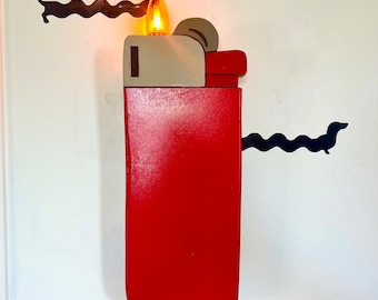 May include: A red and beige lighter-shaped wall lamp with a lit light bulb. The lamp is mounted on a white wall with black dachshund silhouettes.