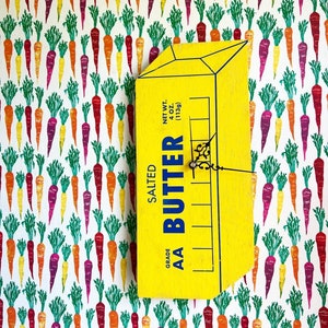 May include: A yellow wooden sign with the words "Grade AA Salted Butter" and "Net Wt. 4 oz. (113g)". The sign is decorated with a carrot pattern.