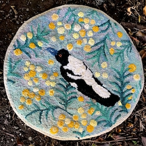 May include: A round, blue and green rug with a white and black bird design. The bird is surrounded by yellow flowers.