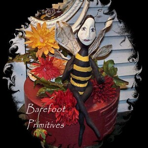 May include: A black and yellow bee with a human-like face sits on a red box with the text "Barefoot Primitives". The bee is surrounded by red and orange flowers.