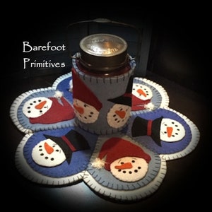 May include: A winter-themed set with a jar cosy and matching coasters. The cosy and coasters feature felt snowmen faces, wearing hats and scarves. The set is in blue, red, and white, with the text "Barefoot Primitives".