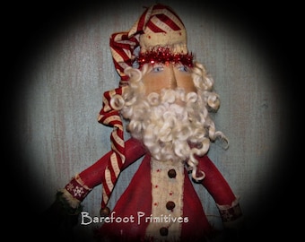 May include: A handmade Santa Claus doll with a red and white striped hat and coat. The doll has a white beard, blue eyes, and a red tinsel garland around the head. The text "Barefoot Primitives" is visible at the bottom.