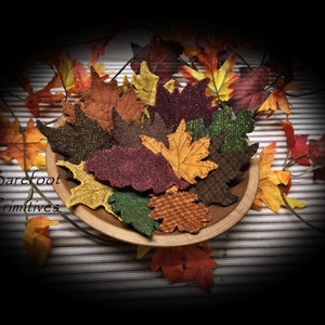 May include: A wooden bowl filled with fabric leaves in autumnal shades of orange, yellow, and burgundy. The leaves display diverse patterns and textures. The image also includes the text "Barefoot Primitives".