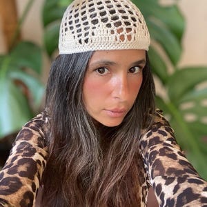 May include: A white crocheted hat with a mesh design. The hat is being worn by a person with long brown hair.
