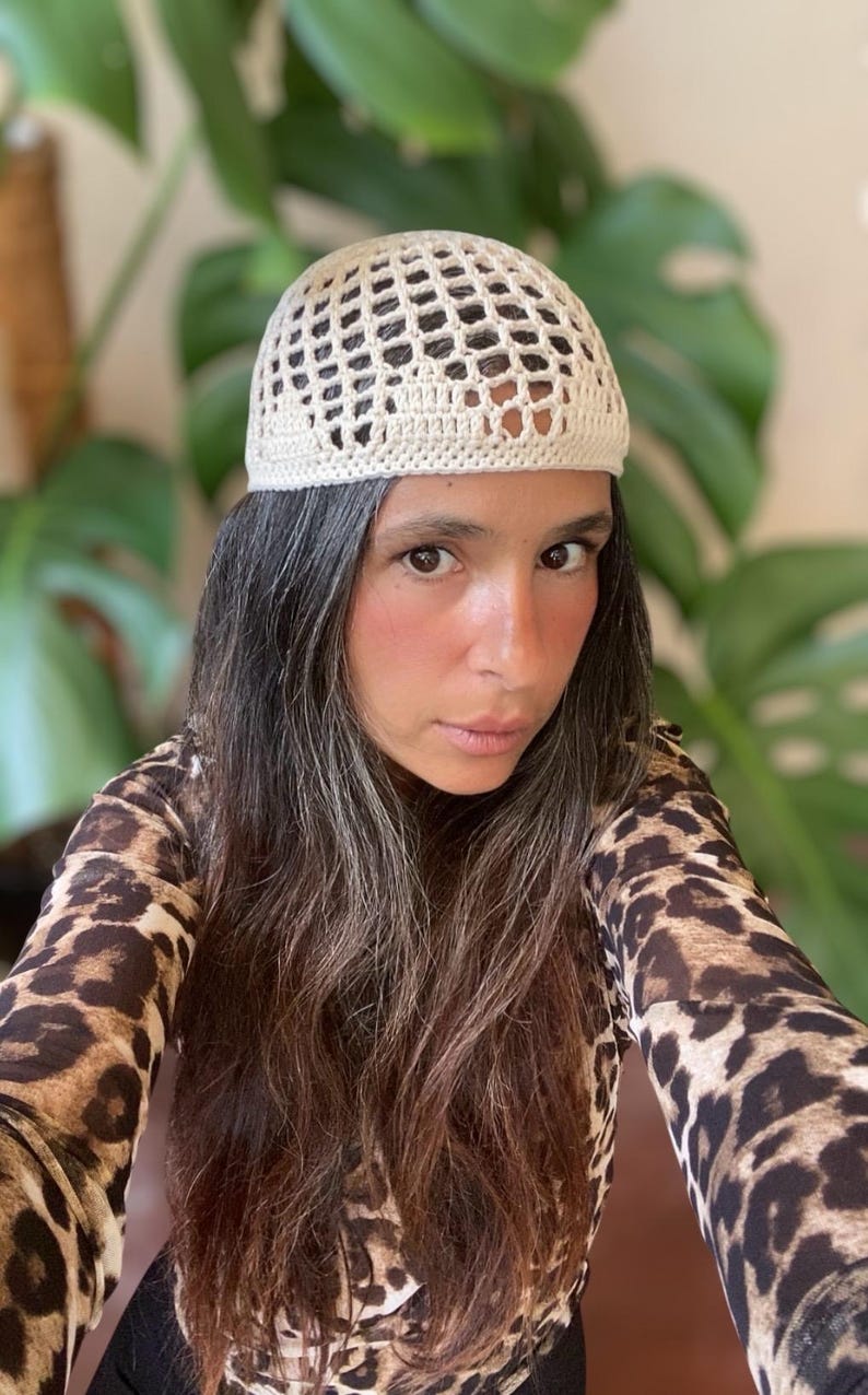 May include: A white crocheted hat with a mesh design. The hat is being worn by a person with long brown hair.