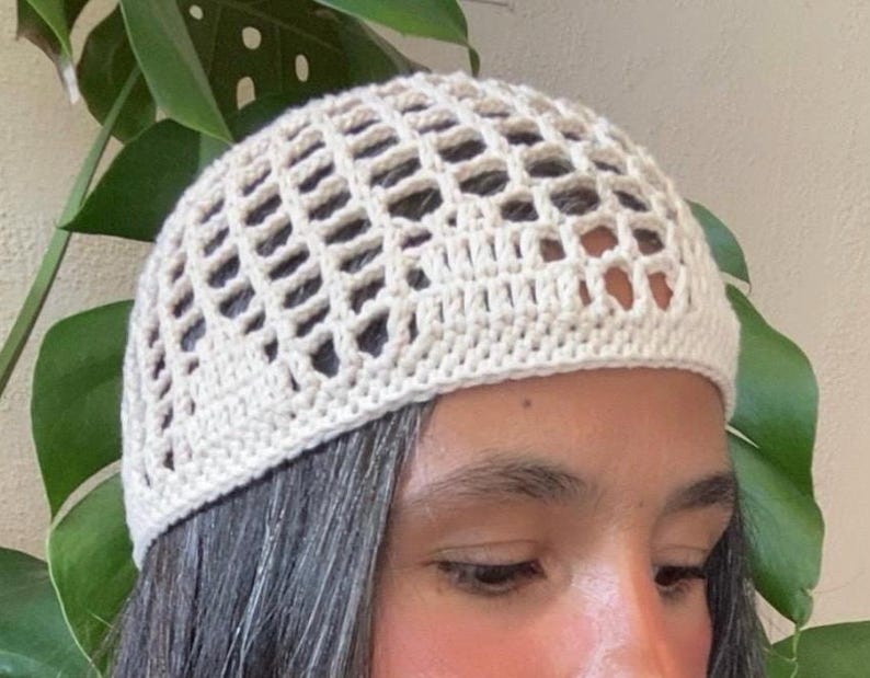 May include: A white crocheted hat with a grid pattern. The hat is being worn on someone's head.