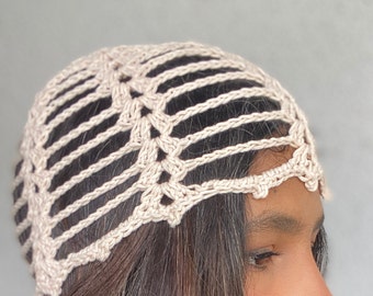 May include: A beige crochet hat with a delicate openwork design. The hat is worn on a person's head, showing the intricate pattern and the soft, airy fabric.