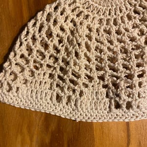 May include: A beige crocheted hat with a delicate openwork pattern. The hat is made with a soft, lightweight yarn and has a comfortable fit.